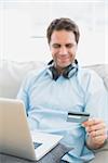 Smiling handsome man sitting on sofa online shopping with laptop at home in the living room