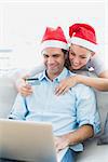 Cute couple in santa hats shopping online with laptop at home in the living room
