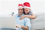 Smiling couple in santa hats shopping online with laptop at home in the living room
