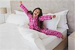 Portrait of a young girl yawning while stretching her arms in bed at home