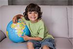 Portrait of a happy young kid with globe sitting in the living room at home