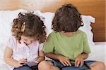 Young boy and girl using digital tablet and cellphone in bed at home