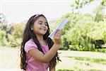 Happy young girl playing with a paper plane at the park