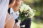 Close-up mid section of a young newlywed couple with bouquet in the park