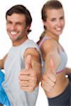 Portrait of a sporty young couple gesturing thumbs up over white background