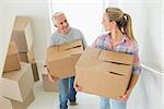 Happy couple carrying cardboard moving boxes in their new home