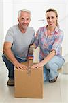 Happy couple sealing cardboard moving boxes in their old home