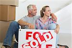 Happy couple sitting on floor with sold sign in their new home