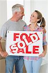 Happy couple standing and holding sold sign in their new home