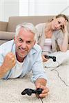 Smiling couple lying on rug playing video games at home in the living room