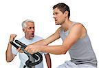 Determined young man on stationary bike with trainer over white background