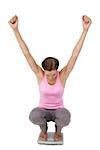 Full length of a young woman cheering on weight scale over white background