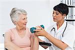 Female physiotherapist assisting senior woman to lift dumbbell in the medical office