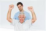 Male physiotherapist assisting senior man to raise hands in the medical office
