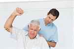 Male physiotherapist assisting senior man to raise hand in the medical office