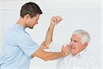 Male physiotherapist assisting senior man to stretch his hand in the medical office
