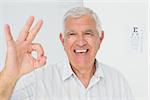 Portrait of a smiling senior man gesturing ok with eye chart in the background at medical office