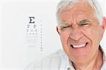 Portrait of a senior man with eye chart in the background at medical office