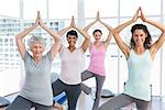 Portrait of a smiling trainer with class standing in tree pose at yoga class