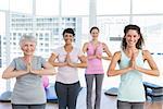 Portrait of a smiling trainer with class standing in namaste pose at yoga class