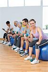 Side view of fitness class with dumbbells sitting on exercise balls in a bright gym