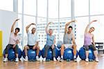 Portrait of fitness class sitting on exercise balls and stretching hands in a bright gym