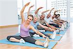 Happy female trainer with class stretching hands at yoga class