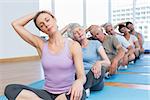 Female trainer with class stretching neck in row at yoga class