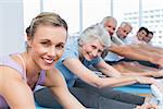 Happy female trainer with class stretching hands to legs at yoga class