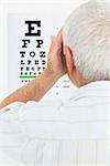 Close-up rear view of a senior man looking at eye chart at medical office