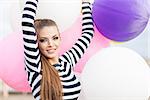 close-up of beautiful smiling girl with smokey eye make up, ponytail hair in black and white striped dress keeps her hands raised holding bunch of multicolored balloons