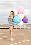 smiling girl in open-back black and white striped short dress and white high top sneakers with bunch of multicolored balloons turns back