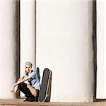 Beautiful girl in short shorts and stockings with skateboard sits on her haunches near  columns on sunny day