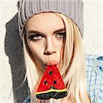 Portrait of sexy blond girl with smokey eye makeup who sucks watermelon lollipop with her plump passionate lips
