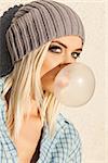 Close-up of beautiful young blond girl in beanie hat blows big bubble from bubble gum