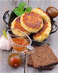 Arrangement of Delicious Chicken Meat Cutlets in Black Saucepan with Brown Bread, Sauce and Vegetables on Wooden background. Top View