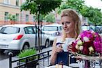 a beautiful young blond girl with blue eyes in summer dress at the table in pavement cafe holding a tea cup is looking at someone