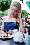 a beautiful young blond girl in summer dress at the table in pavement cafe is having a headache