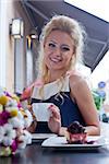 a beautiful young blond girl in summer dress at the table in pavement cafe is smiling for the camera