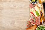 Cheese, prosciutto, bread, vegetables and spices. Over wooden table background with copy space