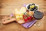Red wine with cheese, olives and tomatoes. Over wooden table background