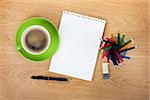 Blank notepad with office supplies and green coffee cup on wooden table. Above view