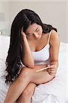 Woman sitting on bed looking at pregnancy test at home in bedroom