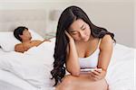 Woman sitting on bed holding pregnancy test as boyfriend sleeps at home in bedroom