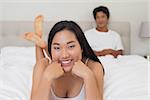 Woman lying on bed smiling at camera at home in bedroom