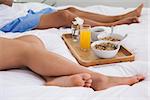 Couple lying on bed with breakfast on a tray at home in bedroom
