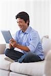 Happy man sitting on couch using tablet at home in the living room