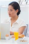 Woman using her laptop at breakfast outside on a balcony