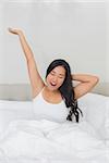 Smiling woman stretching in bed in the morning at home in bedroom