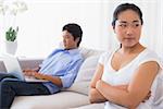 Upset woman sitting on couch while boyfriend uses laptop at home in the living room